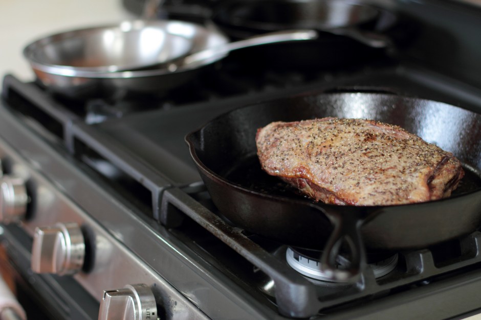 Carne sendo selada em frigideira de ferro preta em fogão doméstico, destacando o preparo culinário.