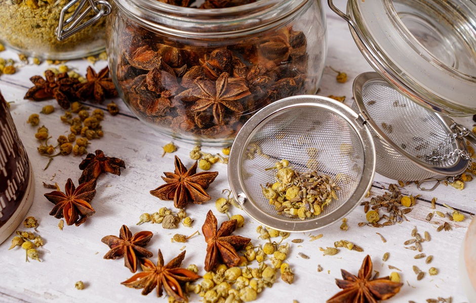 Imagem de especiarias secas e ervas para chás ou temperos, incluindo cravo, canela, hortelã, e outras especiarias, em potes de vidro e escova de chá, ideal para preparar infusões e aromatizar pratos.
