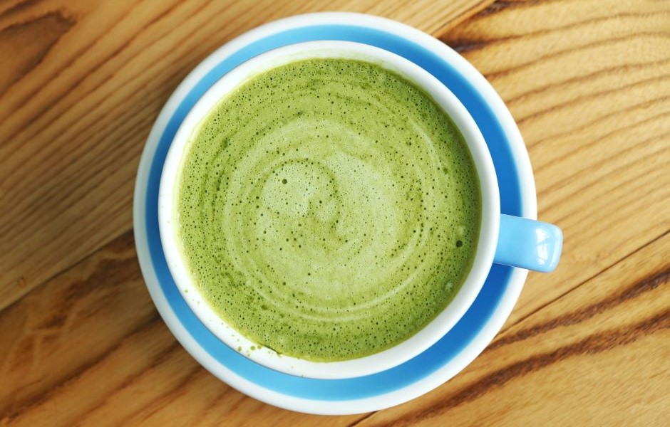 Imagem de uma xícara de chá de matcha com espuma verde vibrante, colocada sobre uma superfície de madeira clara, destacando a cor e a textura do chá de matcha.