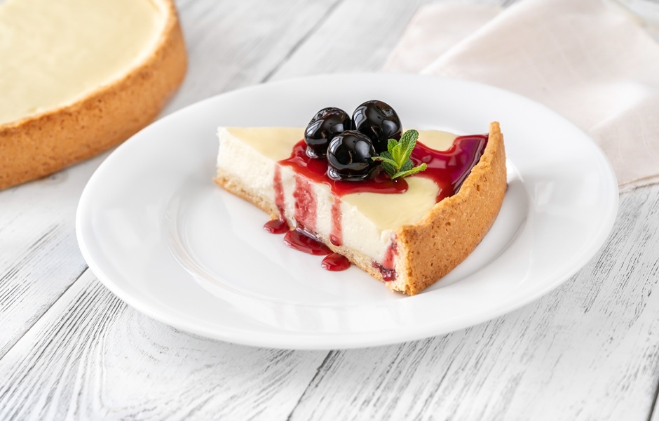Torta de cheesecake com calda de blueberry, decorada com hortelã, em um prato branco sobre mesa de madeira branca