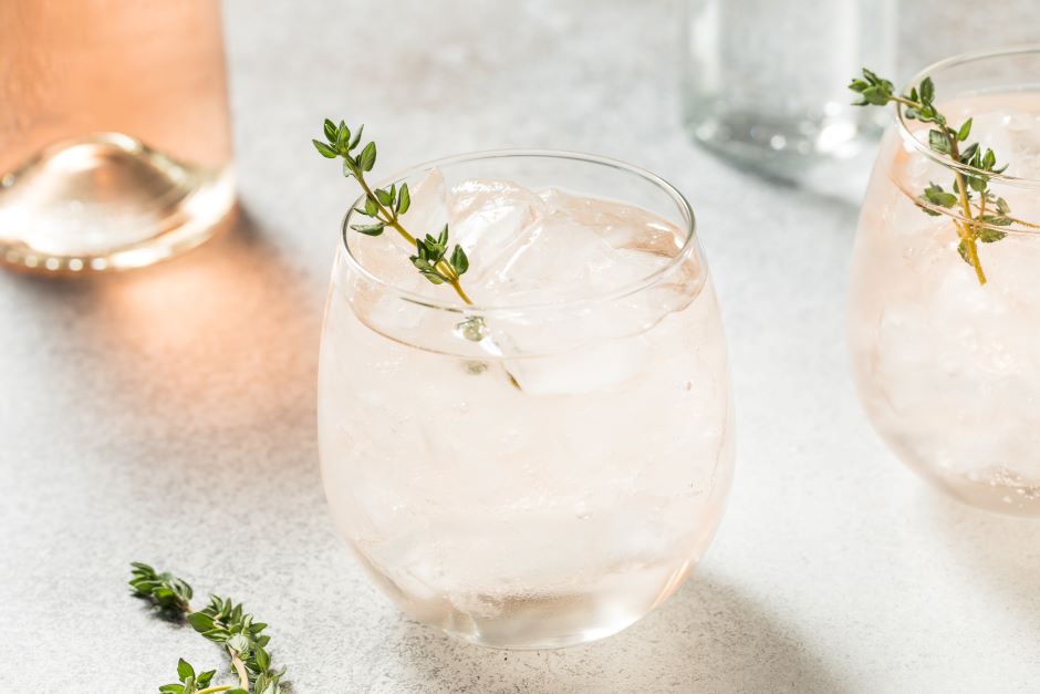 Copo de água com gelo e alecrim, decorado com folhas de alecrim, servido em um ambiente claro e elegante, ideal para refrescar e relaxar.